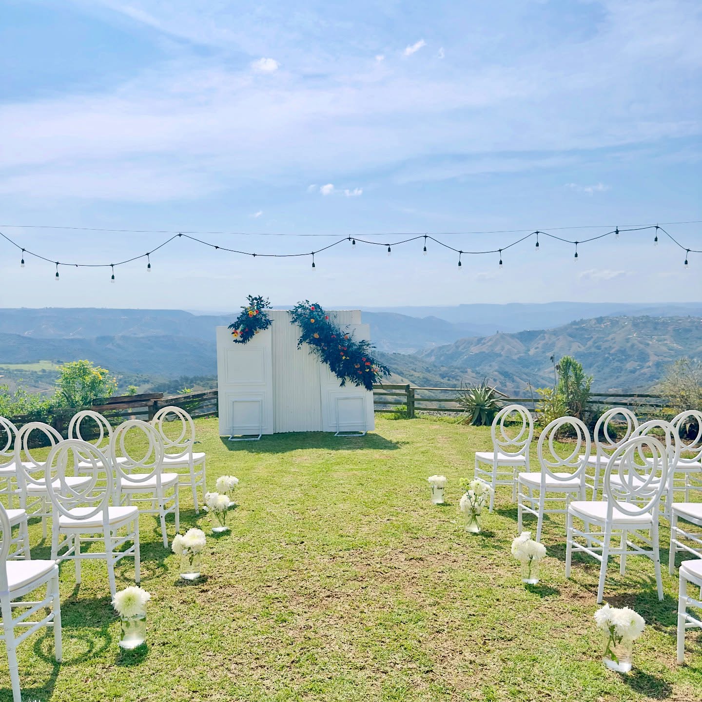 Lawn ceremony with a white panelled backdrop and string lights above the hills