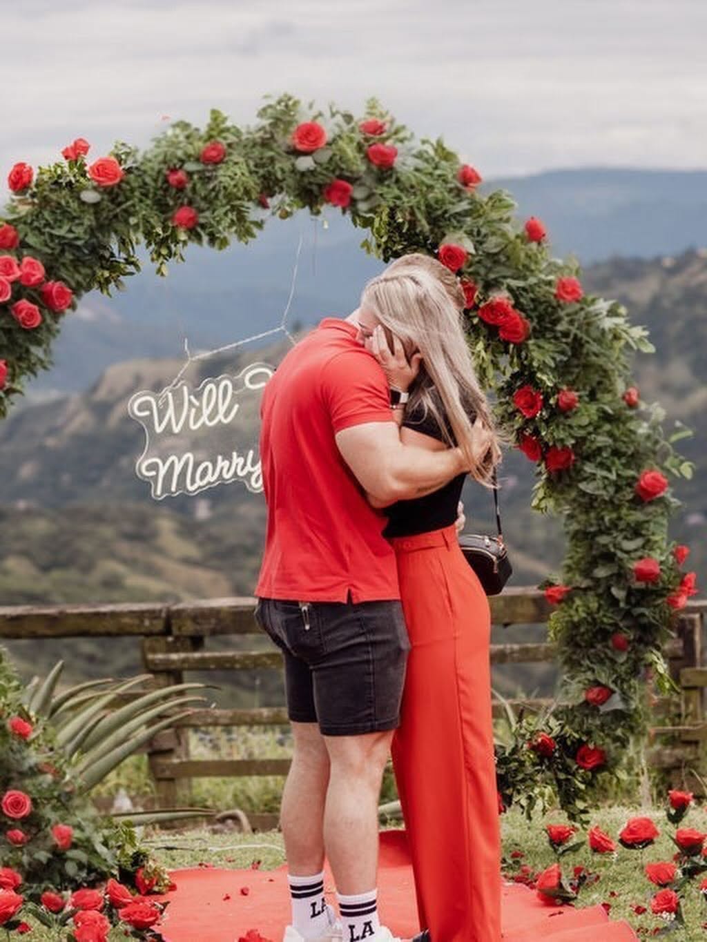 A couple embracing beneath the rose arch after a proposal
