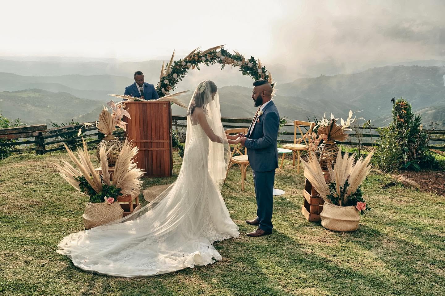 A couple exchanging rings beneath a pampas arch above the valley