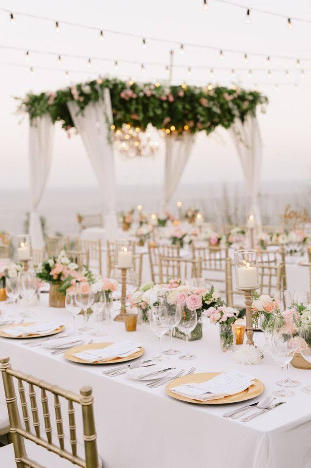 An outdoor wedding reception at Aurum Sky with long tables, gold chairs and a floral arch beneath festoon lights